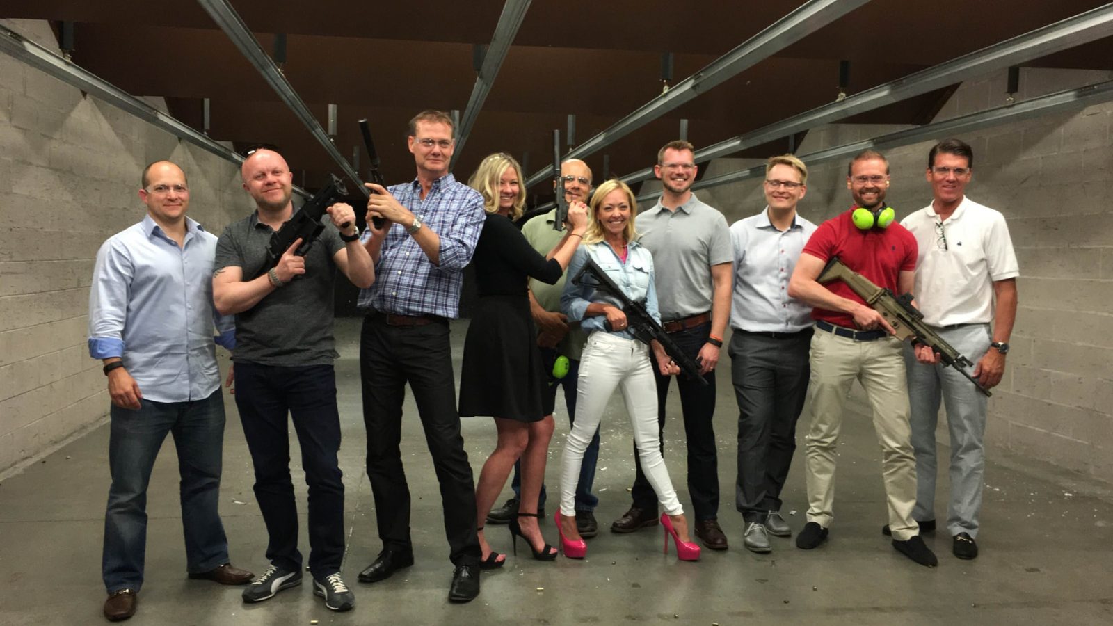 Group of ten adults posing together with firearms in an indoor shooting range bay